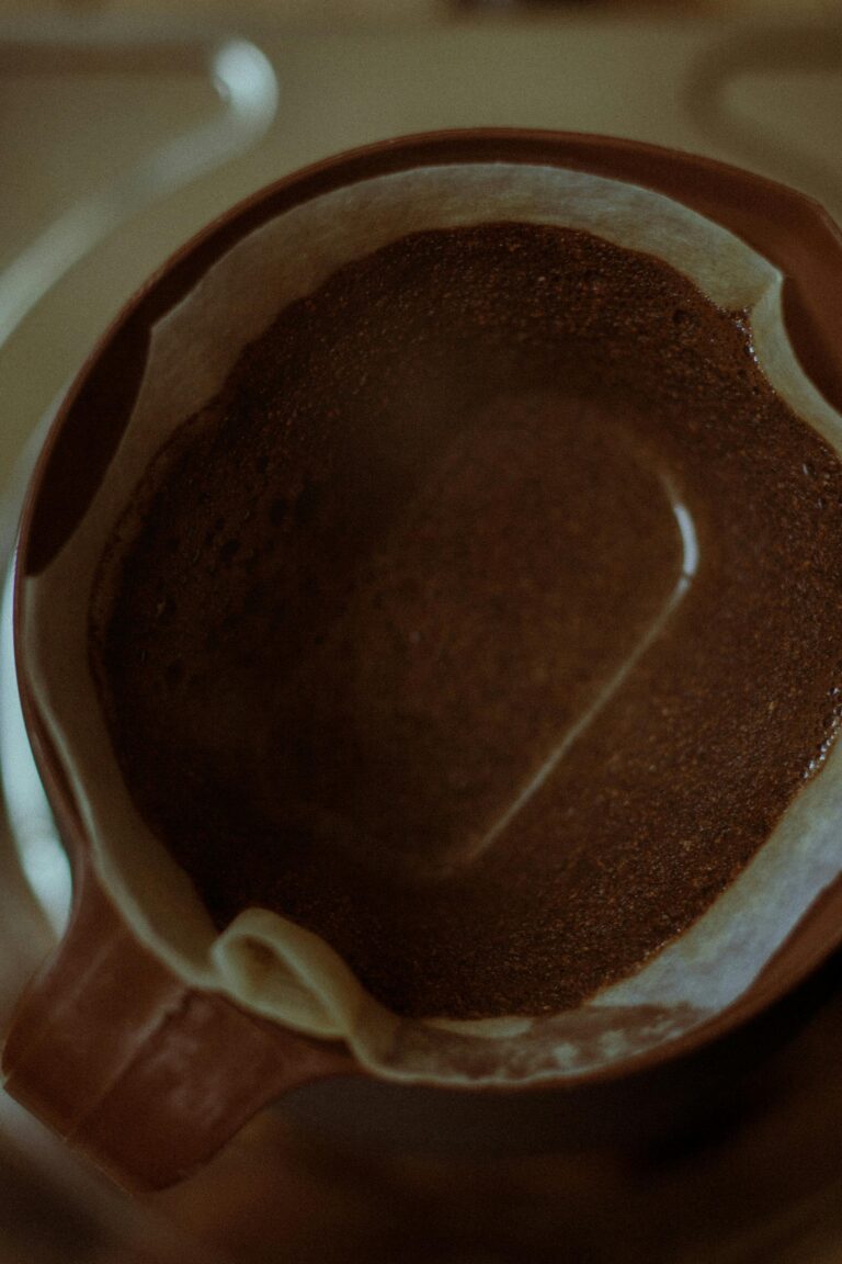 Close-up of brown coffee grounds inside a ceramic cup with a paper filter.
