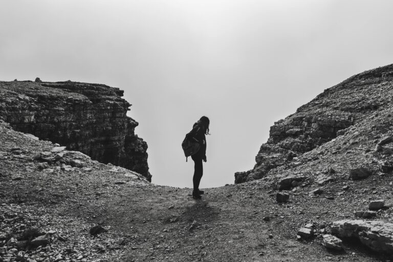 Black and white photo of a woman hiking at Passo Pordoi, capturing a dramatic mountain scene.