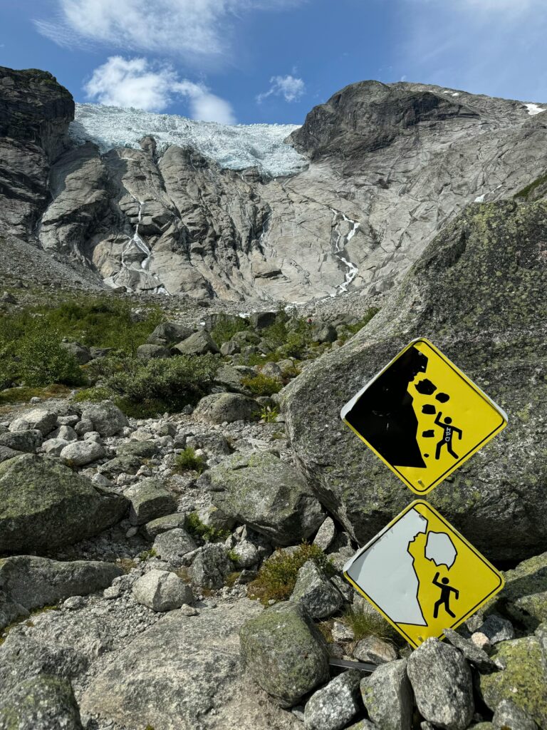 Rocky mountain landscape with warning signs indicating potential rockfalls, under a clear blue sky.