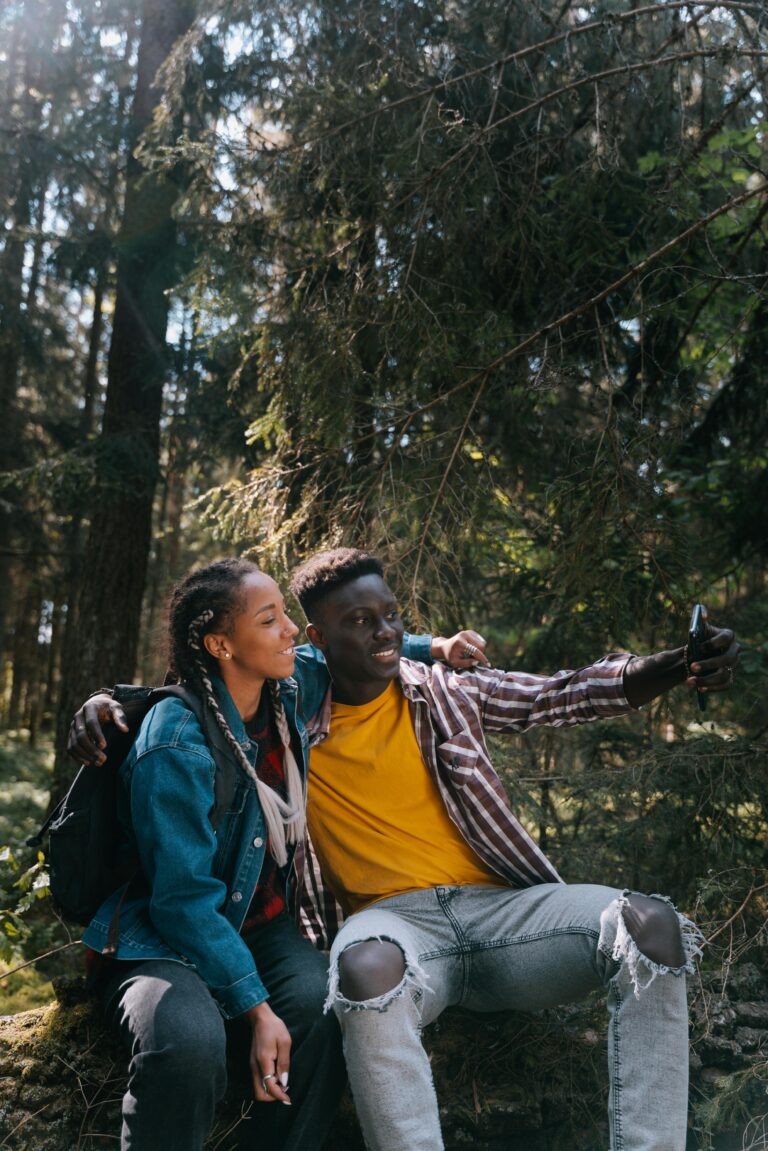 Smiling couple sitting in a forest taking a selfie during a hiking trip.