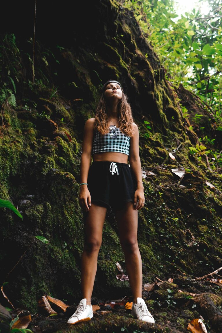 A stylish young woman in trendy attire standing in a lush jungle, exuding confidence.