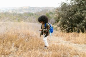 A young boy in a plaid shirt explores a dry field, surrounded by nature.
