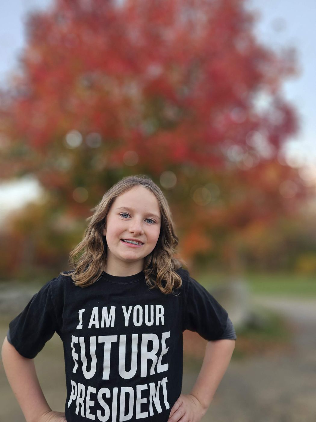 Adeline in an 'I am your future president' shirt in front of a red autumn maple