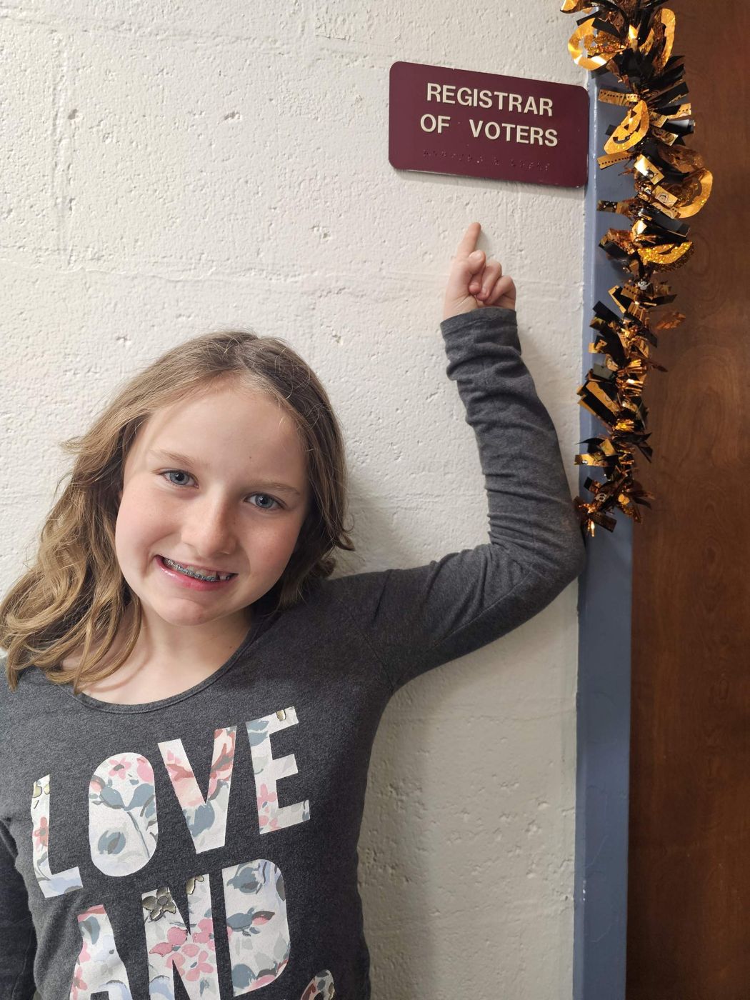 Adeline pointing to the Registrar of Voters sign